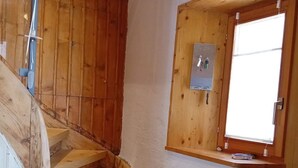 Gradi de fusta que condueix a una habitació amb una finestra i una caixa elèctrica penjada a la paret.