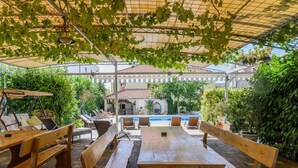 An outdoor patio with wooden benches and tables, a pool, and lush greenery. - mit Whirlpool by Interhome (Trogir)