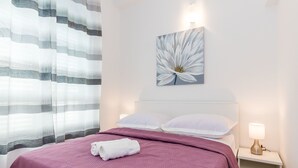 Quarto com cama, mesa de cabeceira, luminária, travesseiro, cobertor e pintura de flores pendurada na parede.
