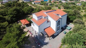 Um edifício branco com telhado de telhas vermelhas, rodeado por vegetação e vista para um corpo de água.