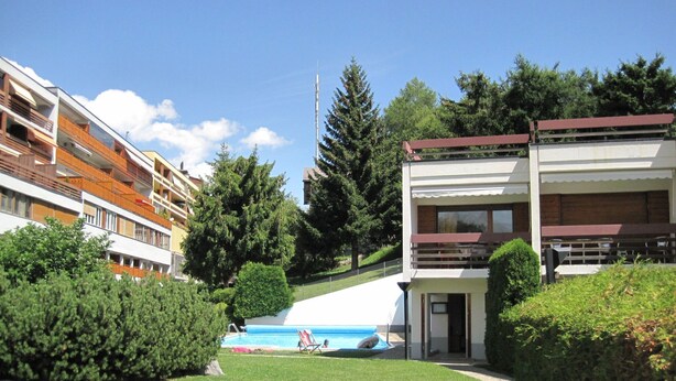 Un bâtiment moderne doté d’une piscine, entouré de verdure et d’autres immeubles.