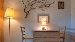 Une pièce avec un bureau en bois, deux chaises, une lampe, un tableau encadré et une décoration en forme de branche fixée au mur.