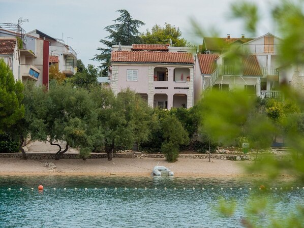 Um edifício à beira-mar com telhado de azulejos, rodeado por árvores e uma praia arenosa.