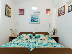 Quarto com cama, duas mesinhas de cabeceira, um criado-mudo, uma planta em vaso e obras de arte na parede.