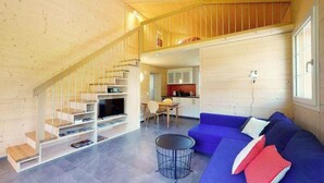 Ein modernes Blockhaus-Interieur mit einer Treppe zu einer Schlafgalerie, einem Wohnbereich mit blauem Sofa, einem Esstisch und einer Küchenzeile.