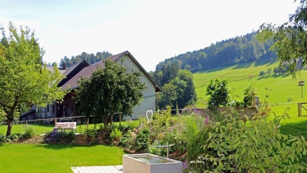 Ein Haus mit Garten, Teich und Blick auf ein grünes Feld und Bäume im Hintergrund.