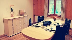 Een eetgedeelte met een houten tafel voor vier personen, een kast met lades en een raam met gordijnen.