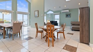 Un comedor amplio con una gran mesa y sillas, un ventilador de techo y ventanas grandes que ofrecen vistas al exterior.