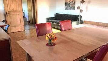 Een eetgedeelte met een houten tafel, rode stoelen en een bloemenvaas. Er is een bank en een schilderij aan de muur.