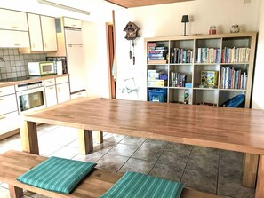 Eine Küche mit einem Holztisch, Bänken, einer Mikrowelle und einem Bücherregal voller Bücher.