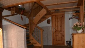 Una escalera de madera que conduce a un segundo piso, un armario de madera con un jarrón de flores y un piso de baldosas.