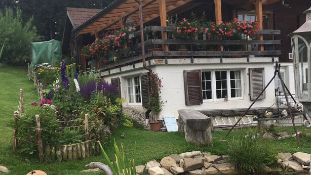 Une maison de campagne avec un jardin, un étang et une balançoire en bois.