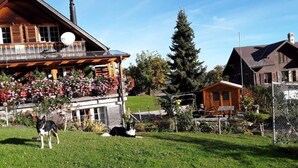 Une maison en bois avec un balcon, une cour clôturée et un petit chalet en bois.