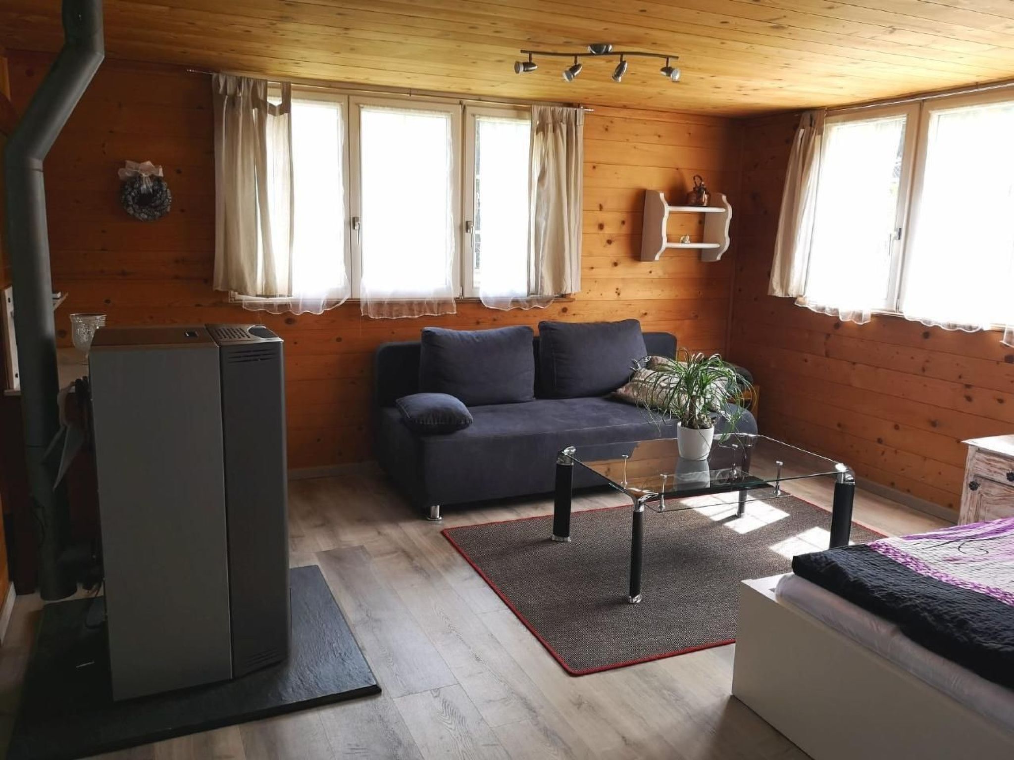 A cozy cabin interior with a sofa, a glass coffee table, a small white dresser, and a refrigerator.