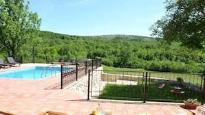 Area piscina con sedie a sdraio e vista su un pendio boschivo.