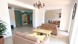 Un ampio soggiorno con un divano color beige, un tavolino e un lampadario. In secondo piano, una zona pranzo con tavolo e sedie.