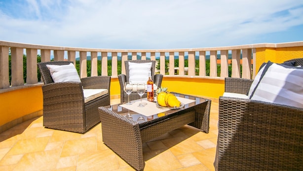 Een terras buiten met rieten meubels, een tafel en een fles wijn.