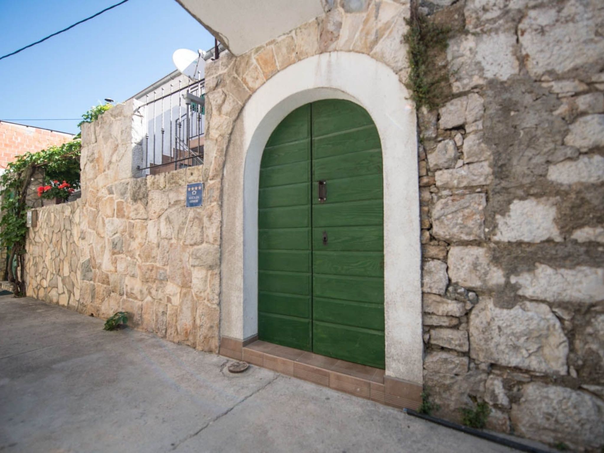 A stone building with a green arched door and a satellite dish on the roof.