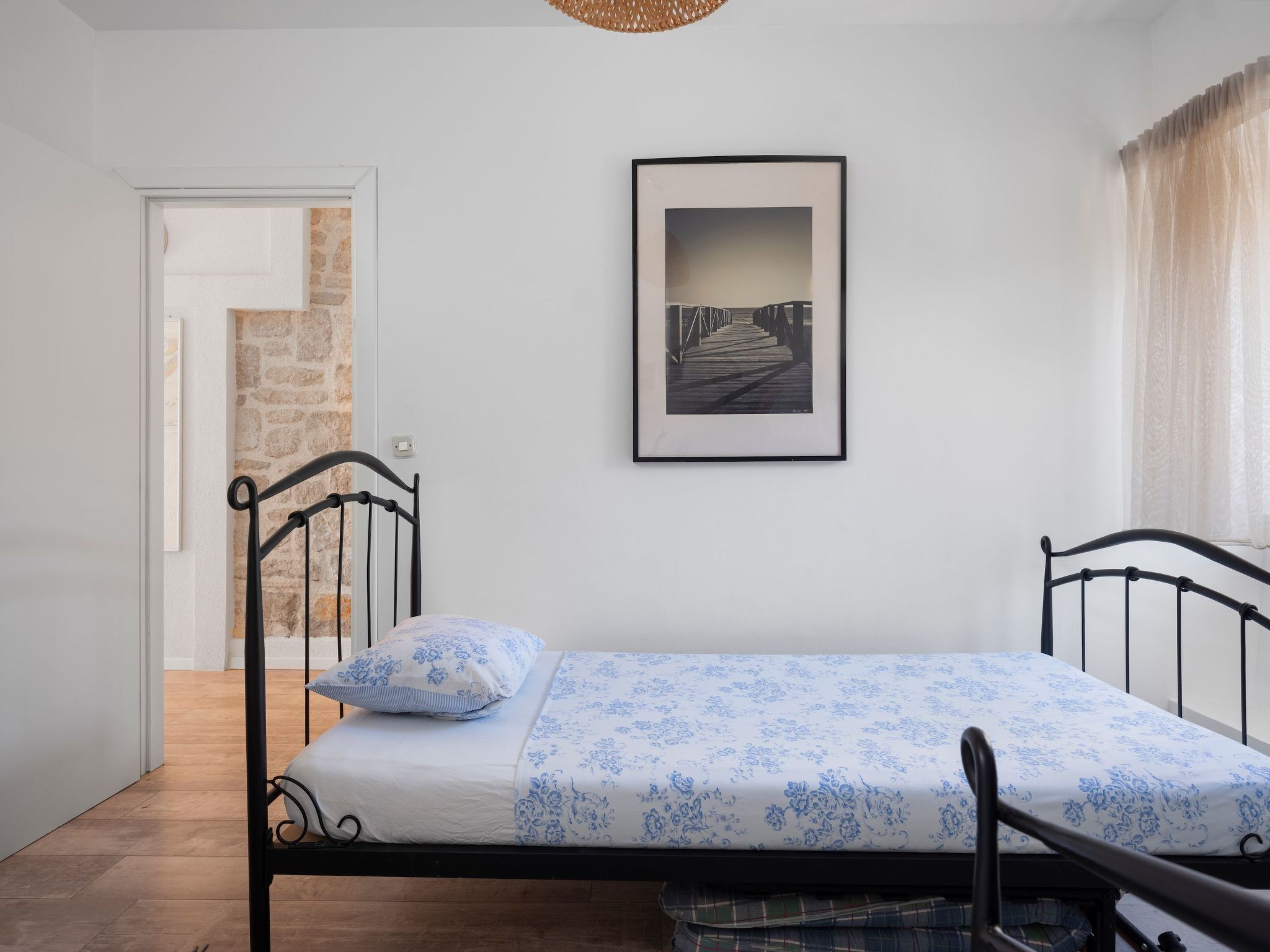 Una cama individual con una colcha estampada, un cuadro en la pared y una puerta que da a una escalera.