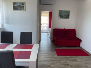 A room with a dining table, two chairs, a red sofa, and a red rug. - Appartement in Fažana mit Grill und Terrasse by Interhome (Fažana)