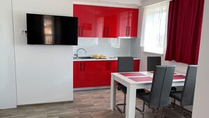 Una cucina compatta con mobili rossi, un piano di lavoro bianco e una TV integrata.