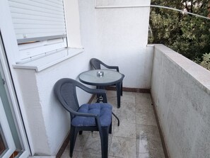 Een klein balkon met een ronde tafel en twee stoelen, een witte gevel en een raam met zonwering.