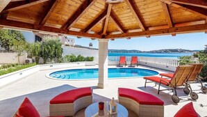 Área externa coberta com piscina, assentos acolchoados vermelhos e vista para o mar.