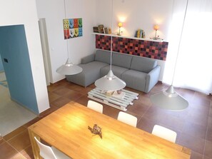 Una sala de estar moderna con un sofá gris, una mesa de comedor de madera y lámparas colgantes.