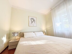 A bedroom with a bed, two bedside tables, a wall-mounted lamp, and a window with curtains. - LacoDeLama mini resort - Wohnung Marta mit Pool by Interhome (Medulin/Ližnjan)