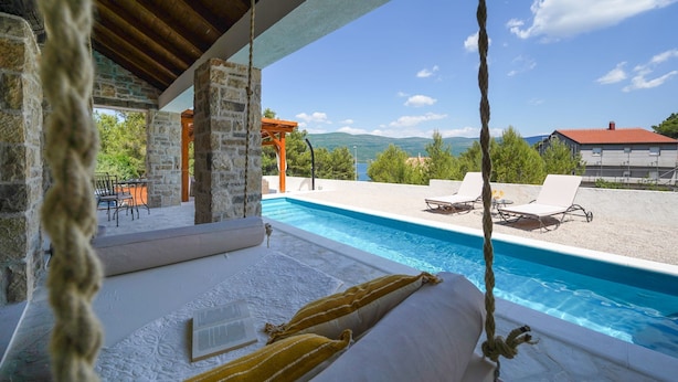 Un espace piscine agrémenté d’un mur en pierre, d’une pergola en bois et offrant une vue sur les montagnes.