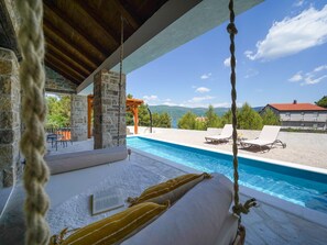 Zona piscina con muro in pietra, una pergola in legno e vista sulle montagne.