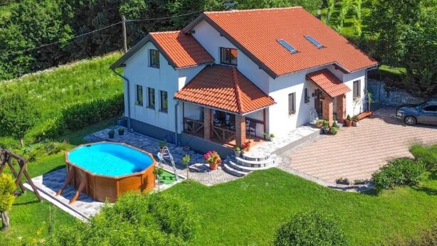 Ein zweistöckiges Haus mit rotem Ziegeldach, einem Swimmingpool und einem gepflegten Garten.