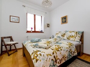 A bedroom with a bed, a chair, a window with curtains, and two framed pictures on the wall.