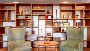 A room with two green armchairs, a round wooden table, and a bookshelf filled with books and decorative items. - Parkresidenz Meilen by Interhome (Meilen)