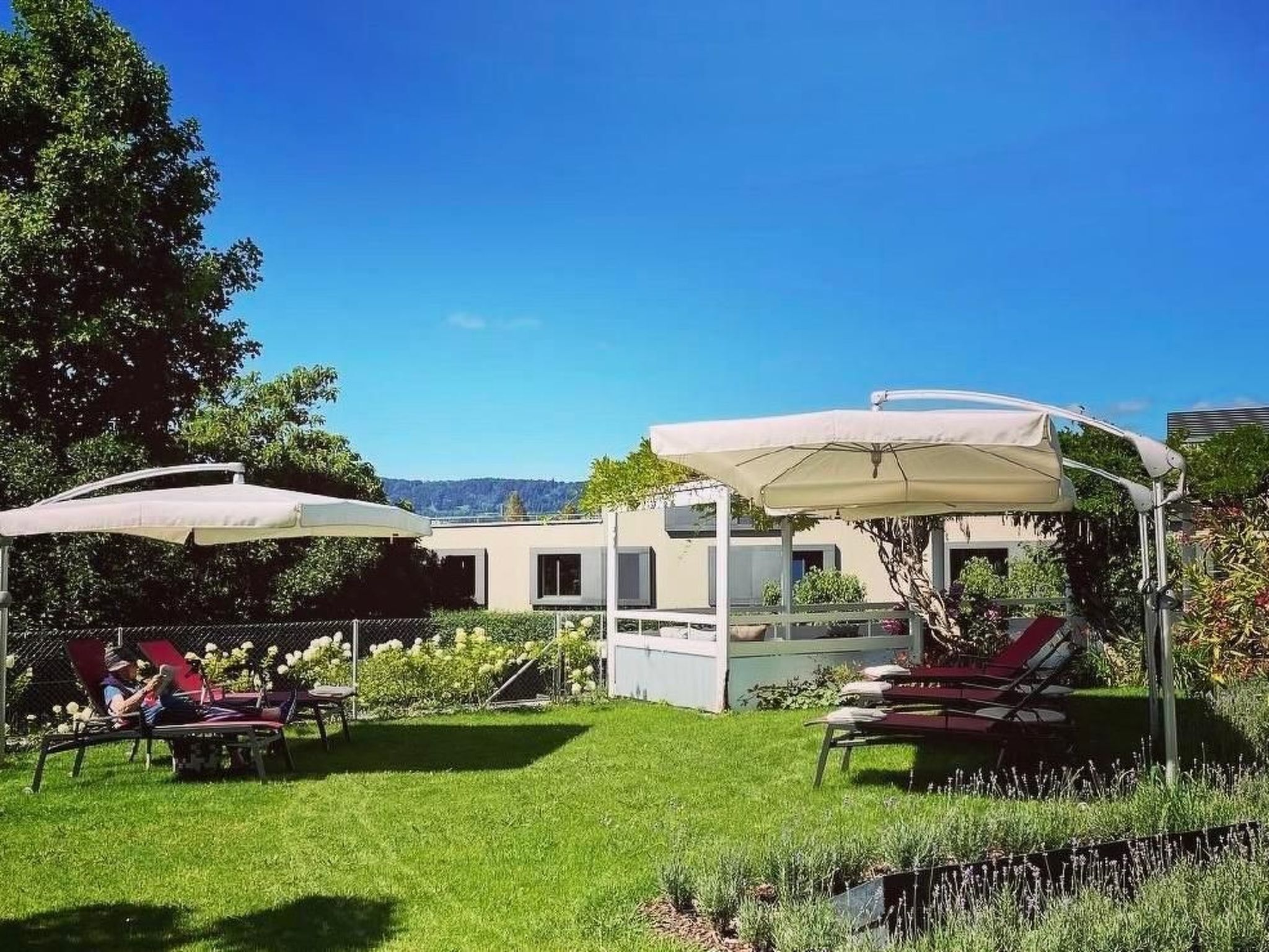 Un espace patio avec des sièges d’extérieur sous des parasols, une pelouse et un bâtiment en arrière-plan.