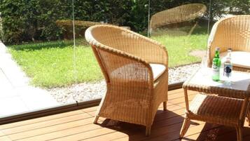 Une chaise et une table en osier, sur une terrasse en bois dotée d’une balustrade en verre.