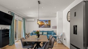 A modern kitchen with a built-in refrigerator, a dining area with a wooden table and chairs, a sofa with teal cushions, and a wall-mounted clock. - Villa Lejla by Interhome (Drenje)