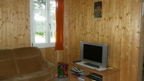A living room with a wooden paneled wall, a sofa, a television on a wooden stand, and a window with curtains. - Ferien im grünen links by Interhome (Haldi b. Schattdorf)
