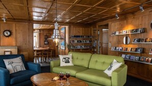 Un accogliente soggiorno con un divano verde, una poltrona blu e un tavolino in legno con calici di vino.