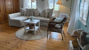 Una sala de estar acogedora con un sofá blanco, un sillón de mimbre, una mesita blanca y suelo de madera.