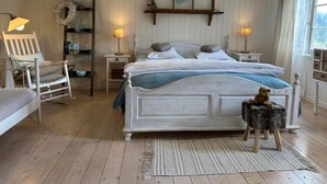Un dormitorio con una cama grande, dos mesitas de noche, una silla, una estantería con libros y una lámpara colgante.