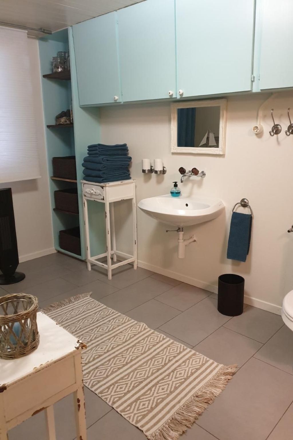 A bathroom with a sink, mirror, towel rack, and a small table with a basket.