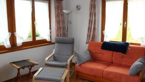 Ett mysigt rum med en grå fåtölj, ett litet bord och en orange soffa med en pläd.