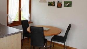 En matplats med ett runt träbord, två svarta stolar, ett träskåp och ett fönster med gardiner.