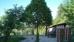 Ett rustikt utomhusområde med en grusgång, en träpergola och en hög med ved.