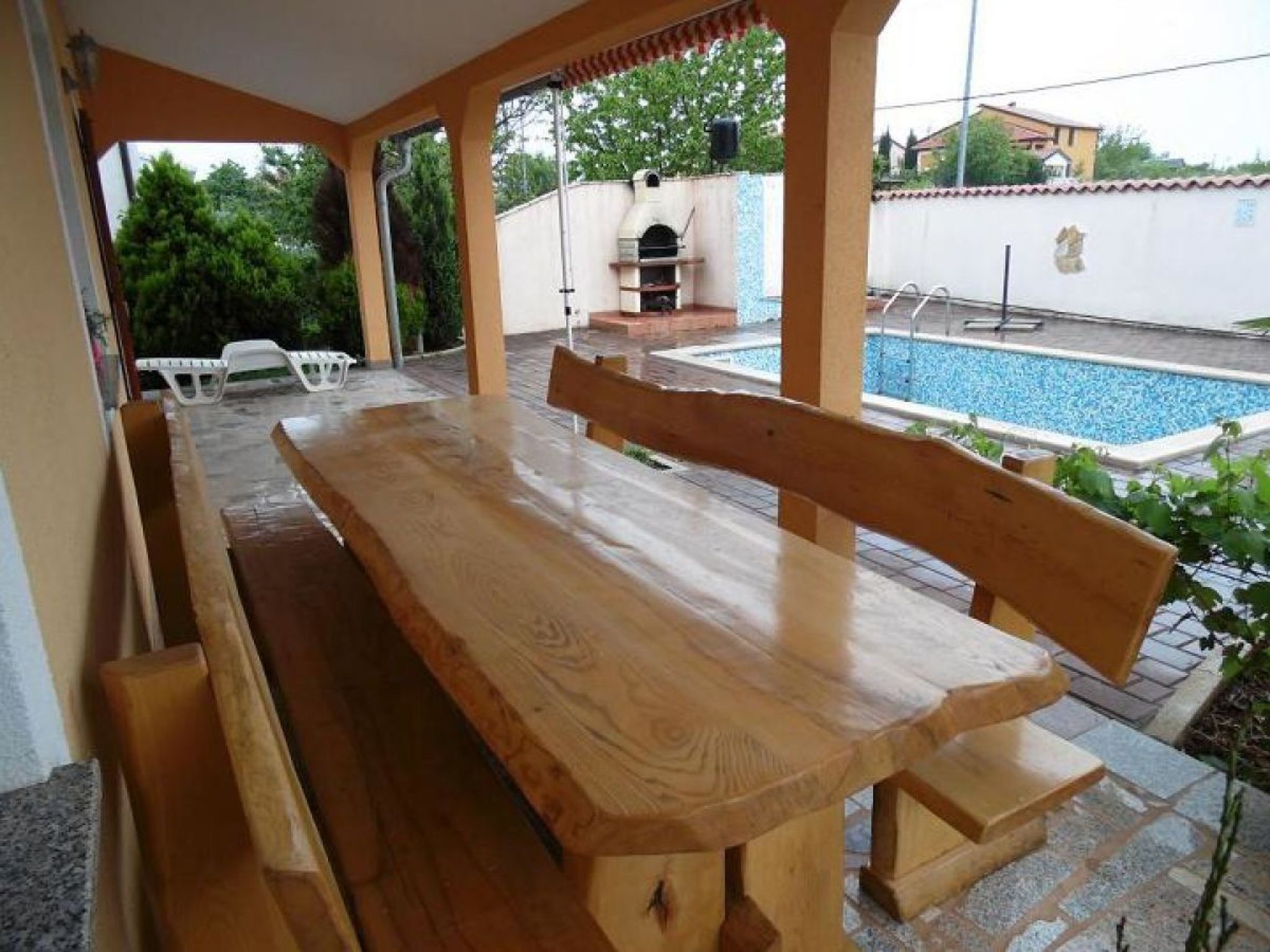 A wooden bench and table set up on a patio with a pool in the background.