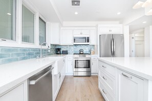 A modern kitchen with white cabinetry, stainless steel appliances, and a blue-tiled backsplash. - Remodeled Oceanfront Home Right on 36th Street Beach and the Boardwalk! (Newport Beach)