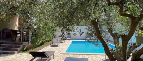 Una piscina con sillones de descanso y un sendero de piedra.