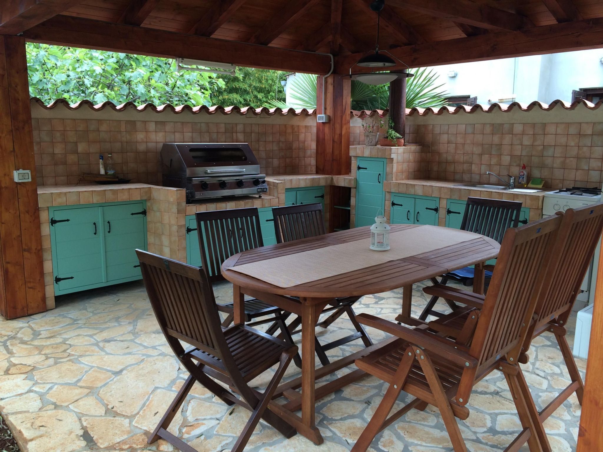 An outdoor kitchen with a grill, tiled backsplash, and a table with chairs.