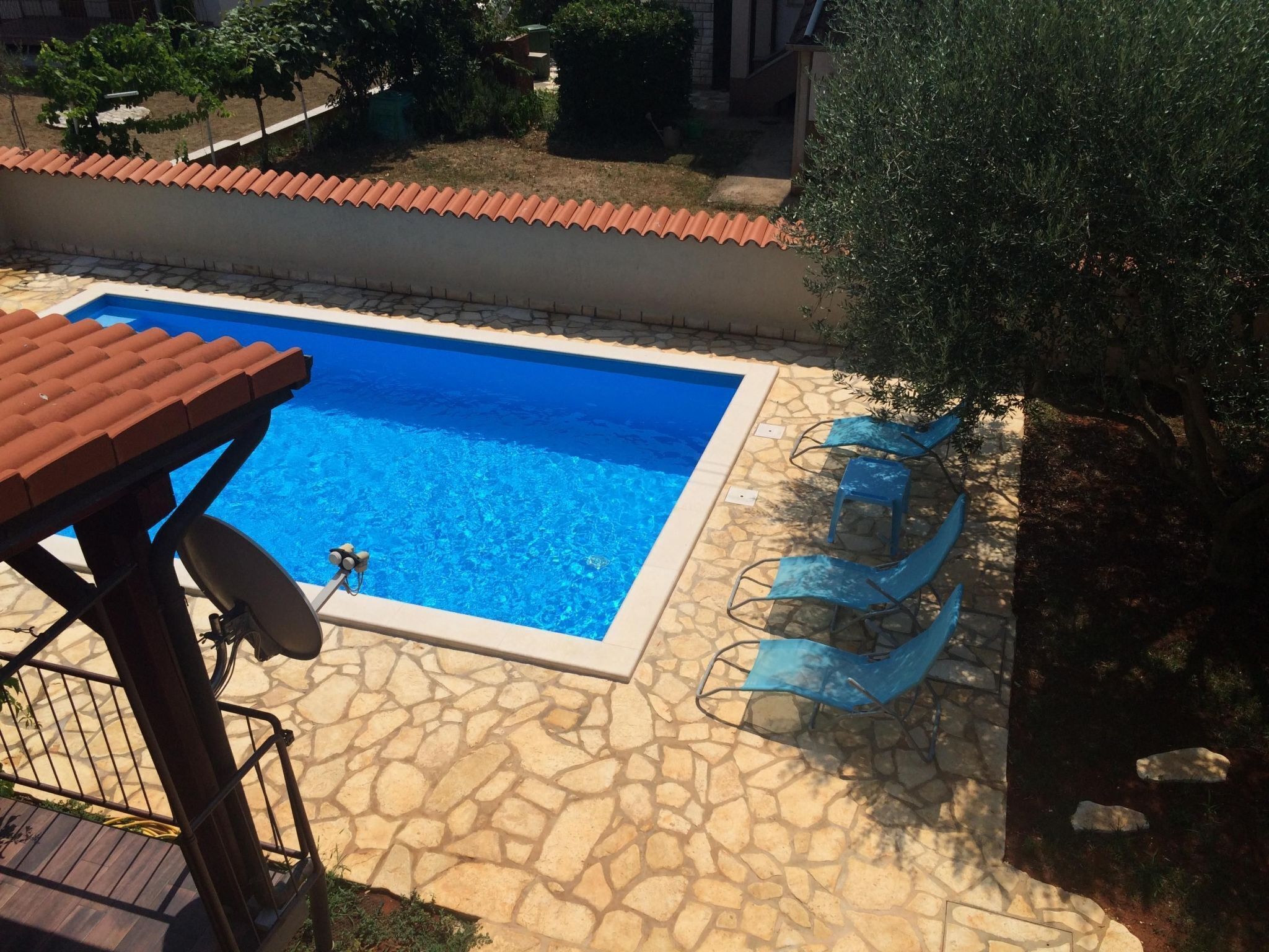 Une piscine avec des carreaux de pierre, une pergola et une chaise au bord de la piscine.